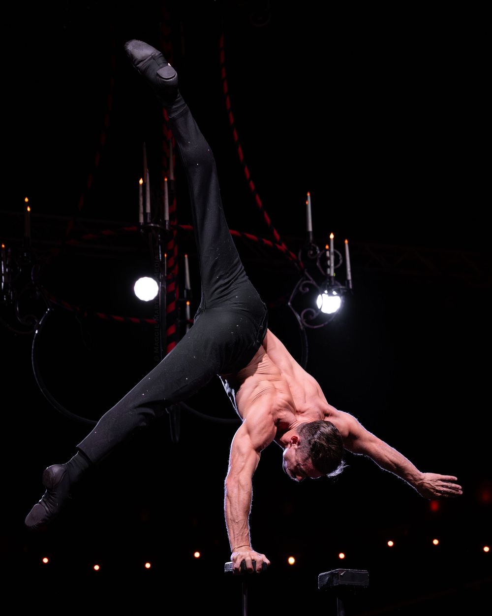 Performer executes an acrobatic aerial sequence in a darkened theater with dramatic lighting effects.