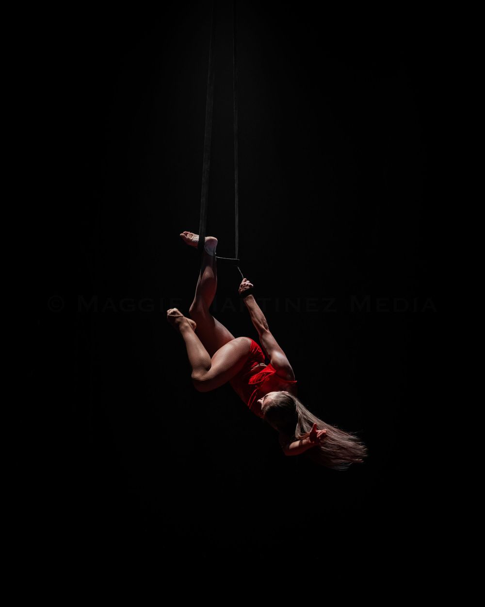 Aerial performer Lindsay Culbert-Olds in red costume dramatically suspended in aerial straps against dark background.