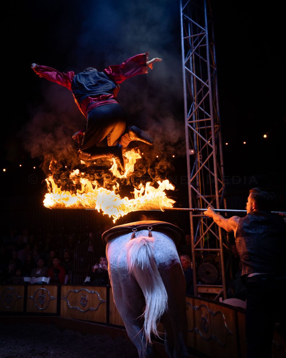 Performer leaps over dramatic fire display during nighttime circus act.