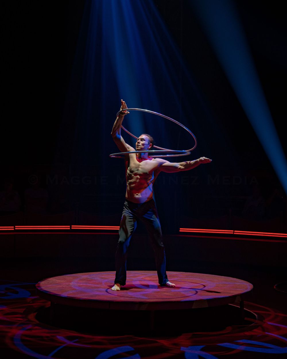 Performer Anton Monastyrsky with hula hoops creates dynamic silhouette under dramatic stage lighting.