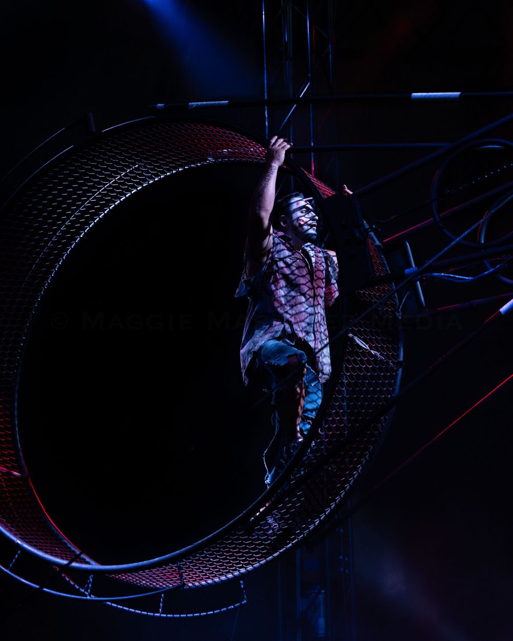 Circus performer Carlitos Wheel gracefully maneuvers inside illuminated metal wheel during show.