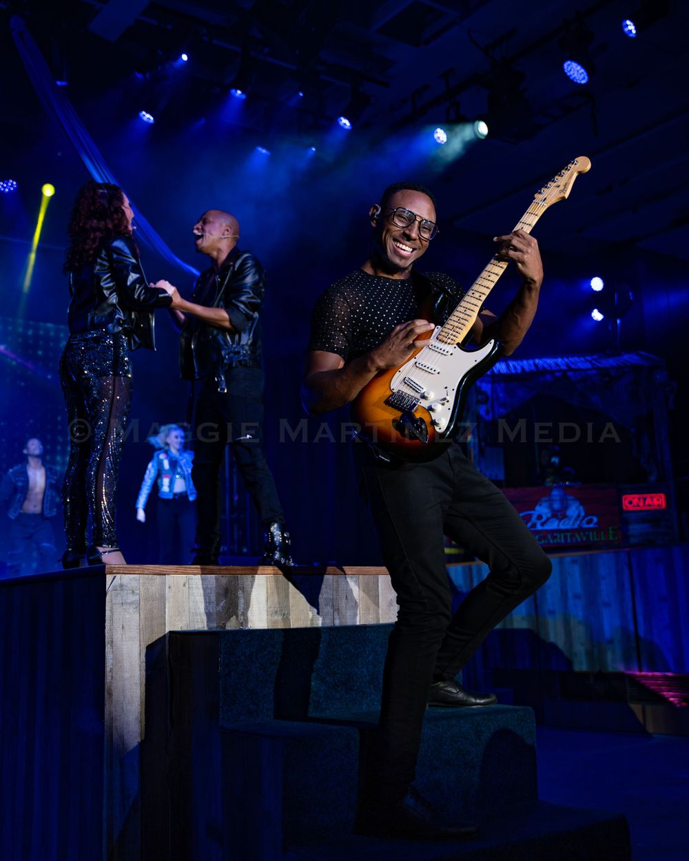 Musicians performing energetically on stage under blue concert lighting.