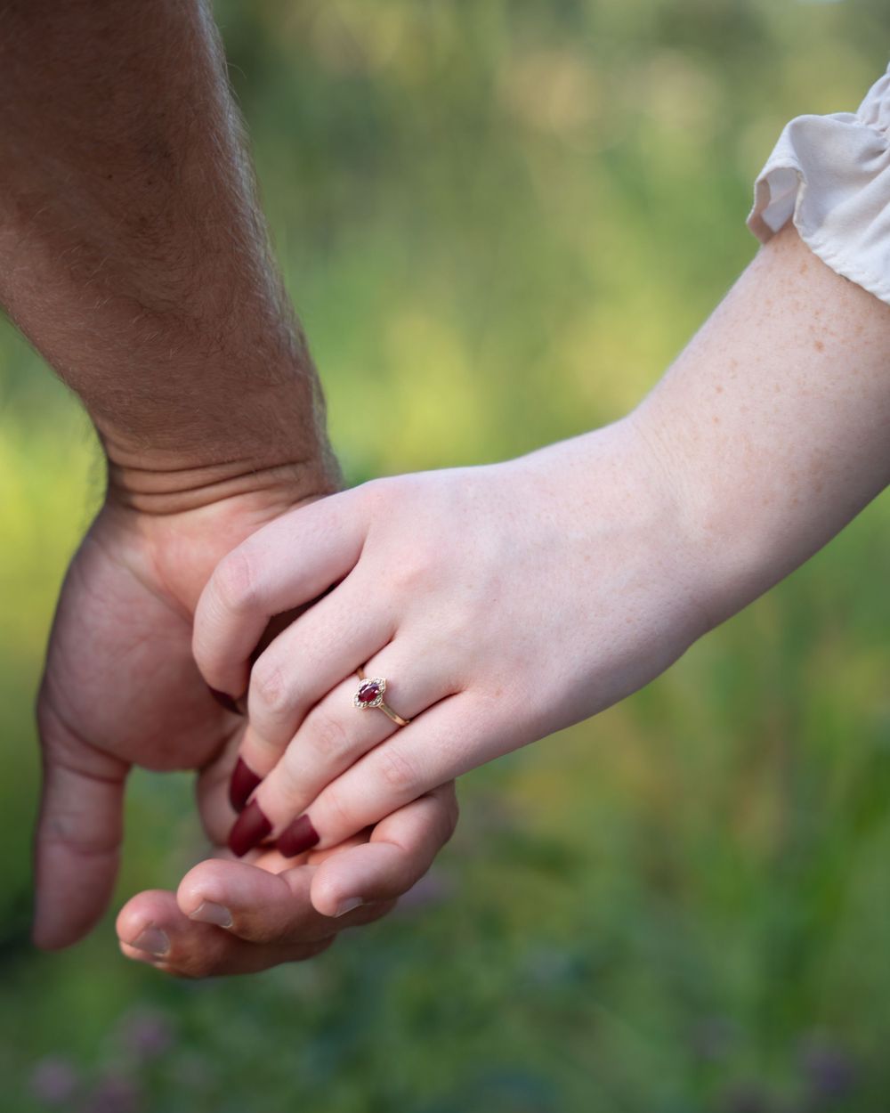 Close-up of holding hands with engagement ring in outdoor setting.