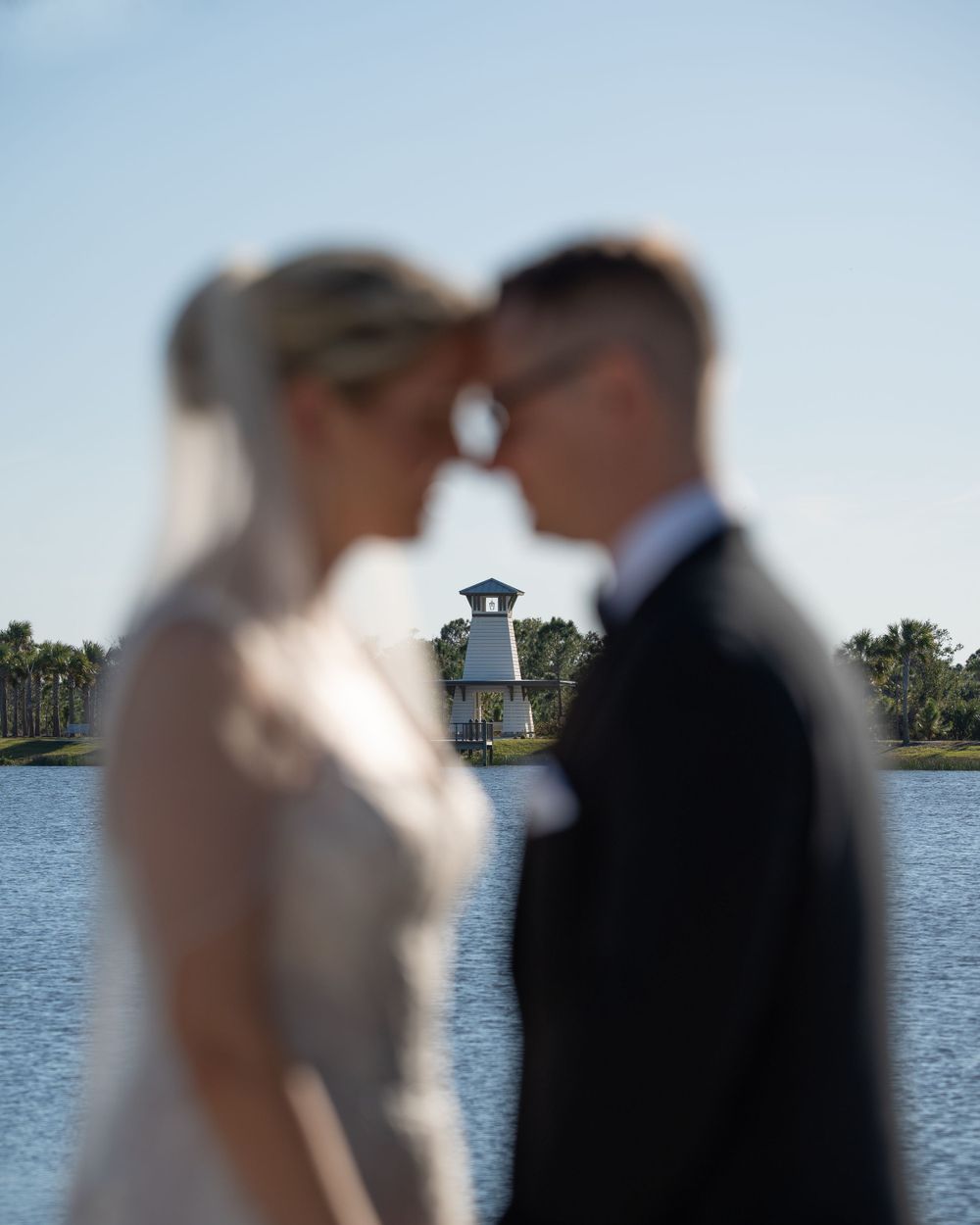 Creative wedding photo with lighthouse in focus between blurred couple.