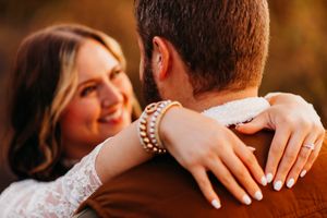 A couple in an intimate embrace, with a glittering bracelet visible on the bride's wrist during a sunset photoshoot.