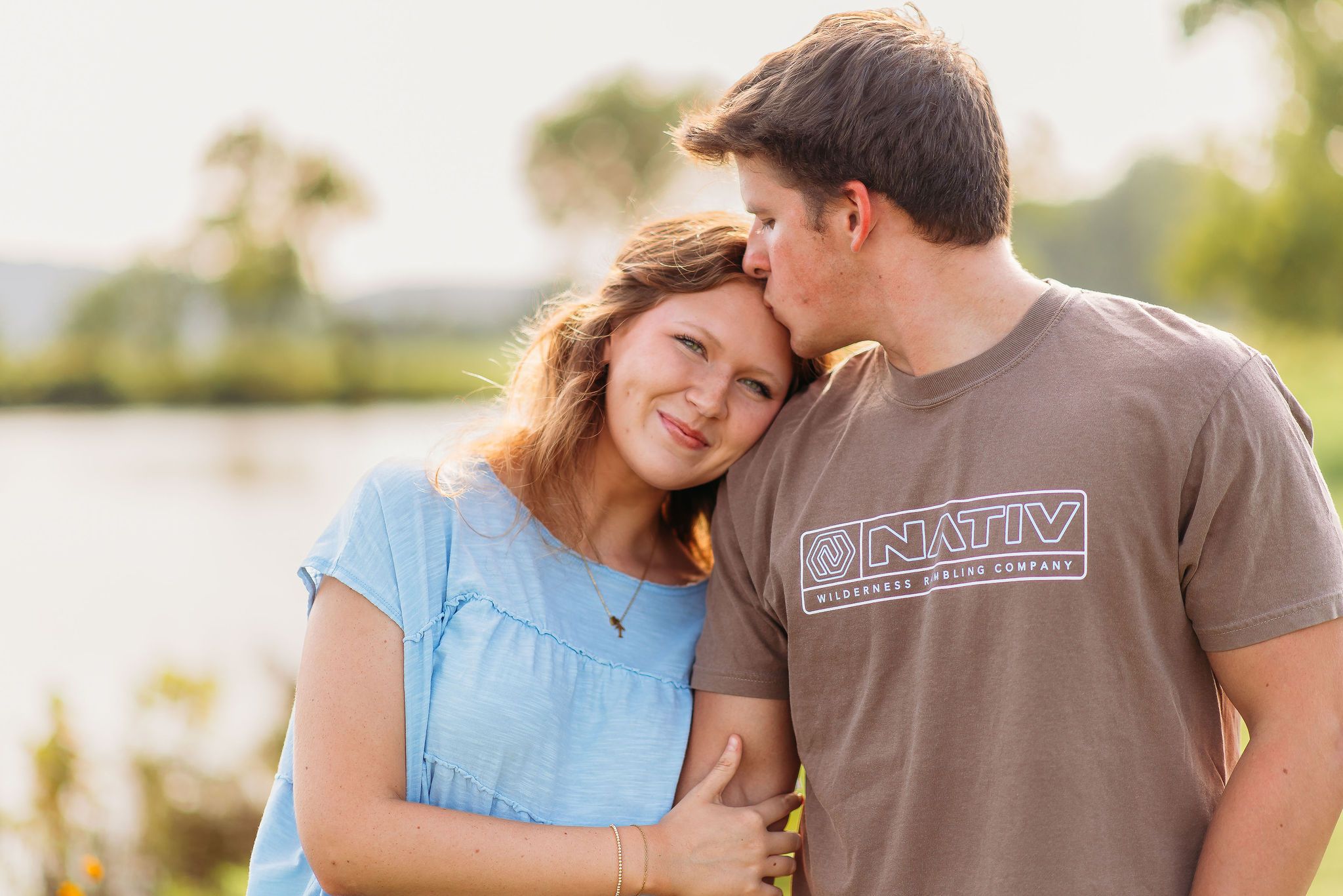 A couple sharing an intimate moment at sunset by a lake, with soft natural lighting and warm expressions.