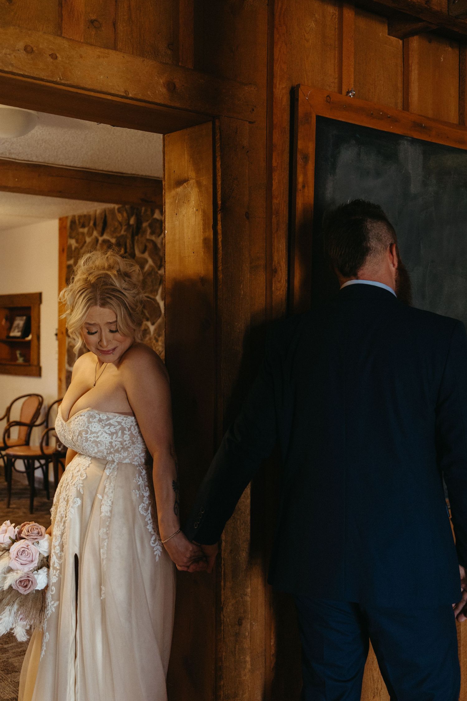 A bride in a lace dress walks through a rustic wooden hallway.