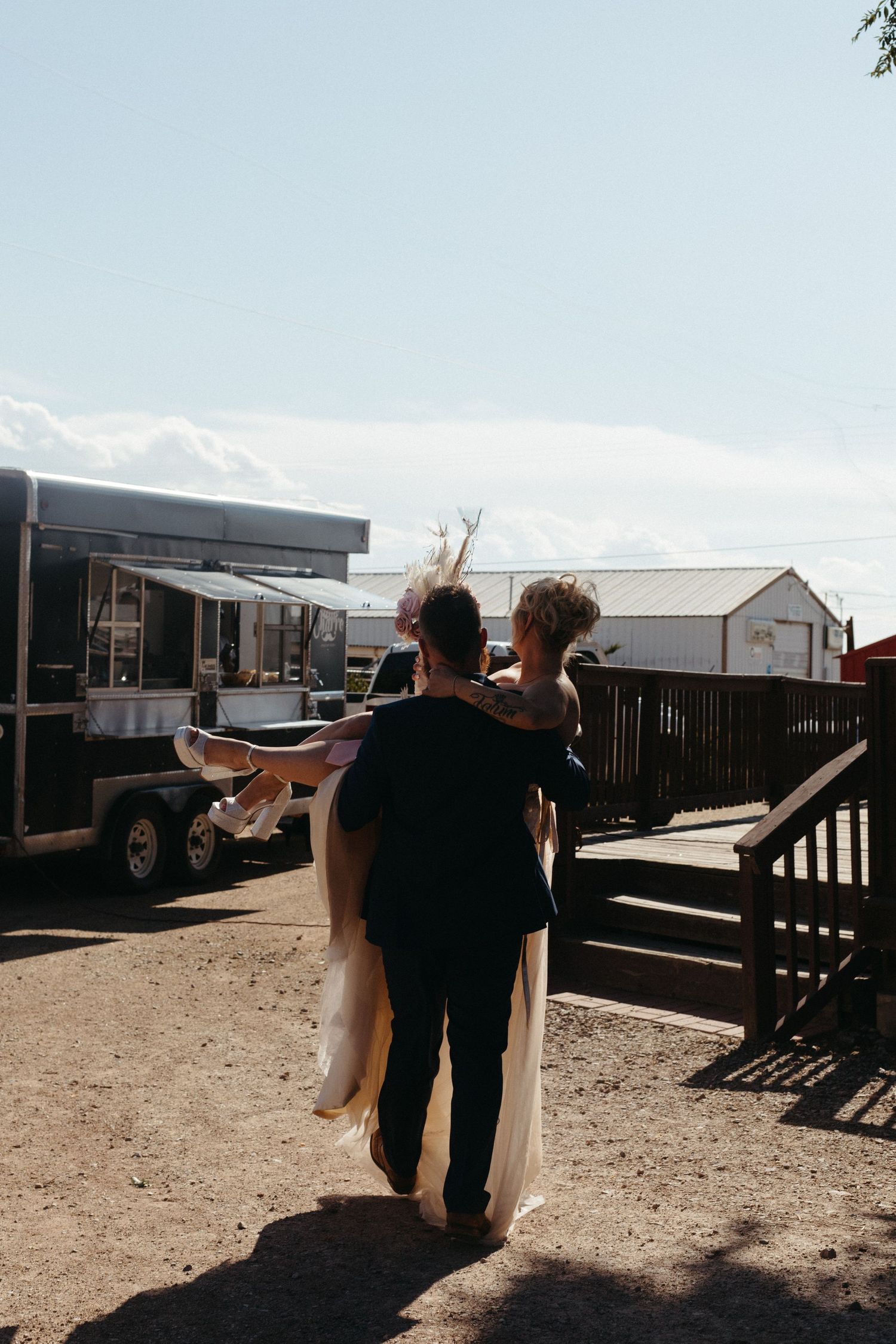 A newlywed couple walks together in bright sunlight outside.