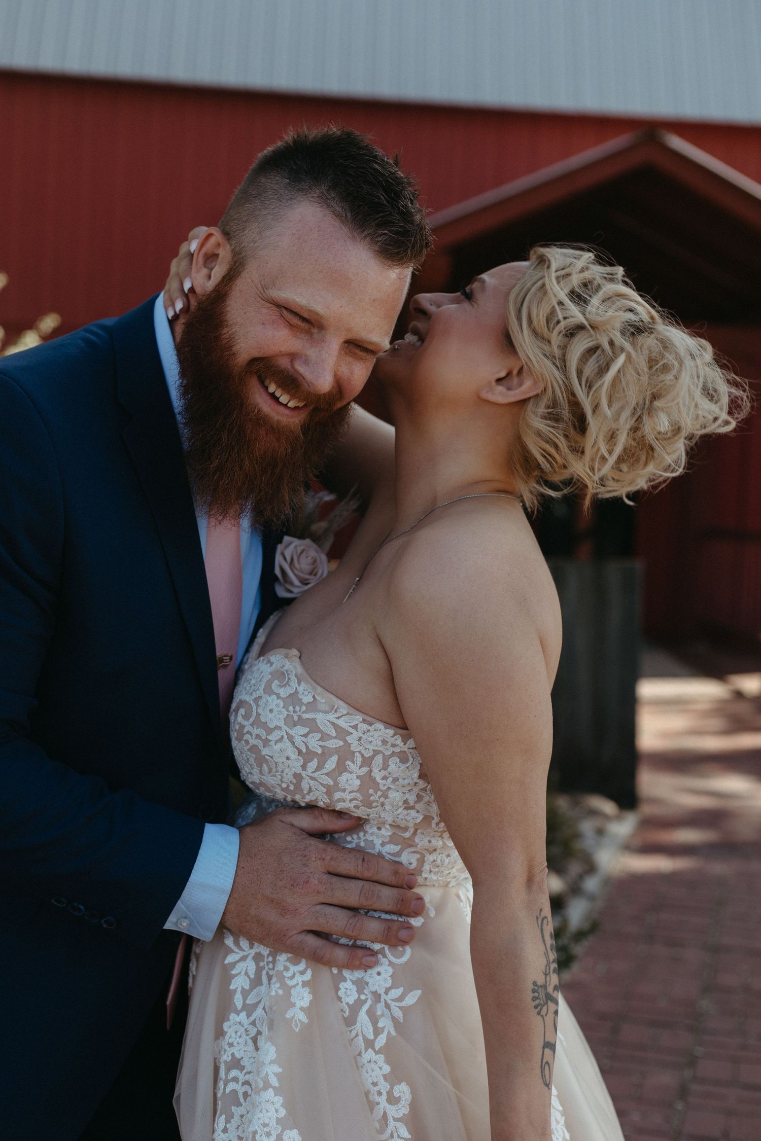A romantic wedding moment captured near a red barn with a couple in formal attire.