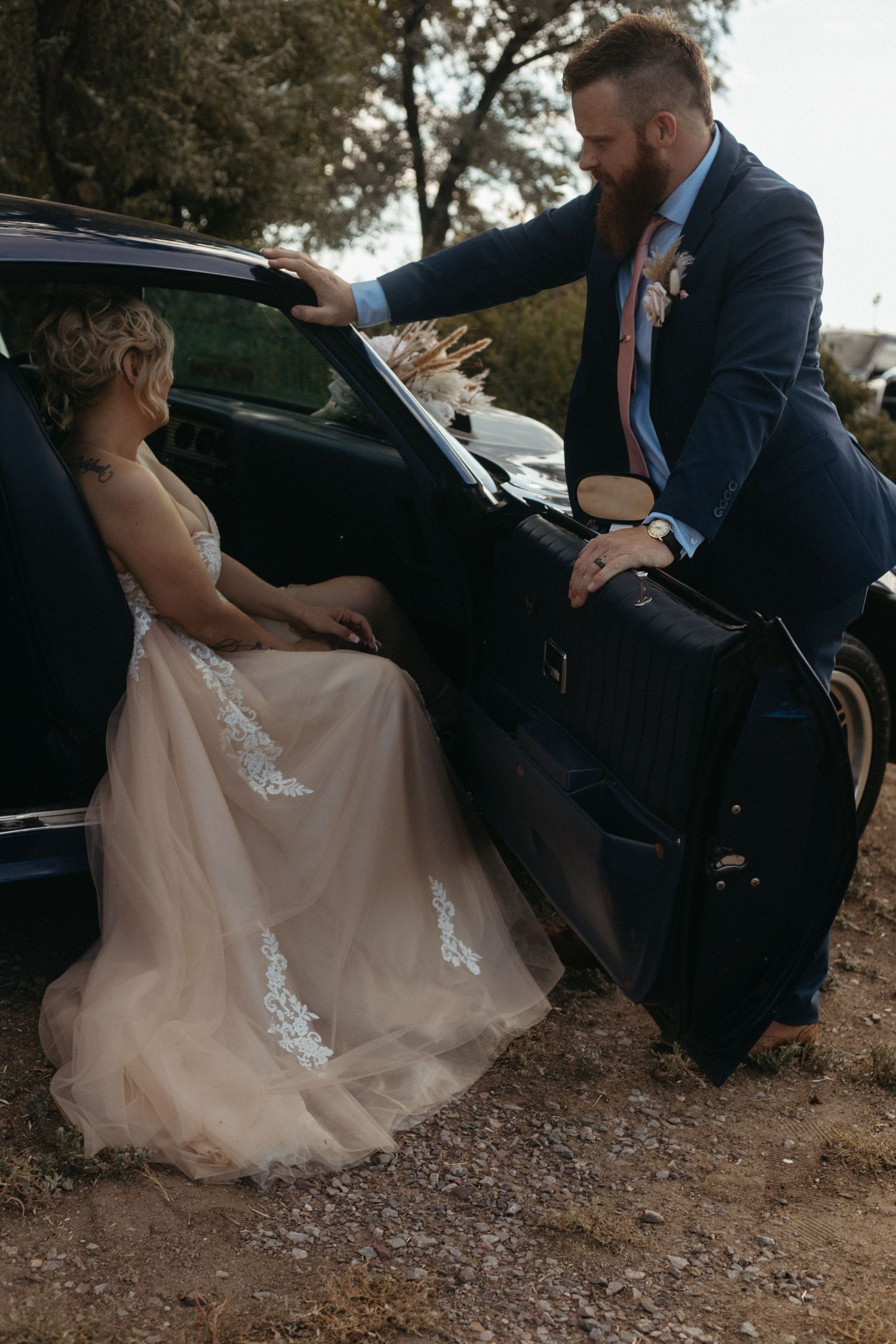 A couple shares a tender moment by a classic car during their wedding photoshoot.