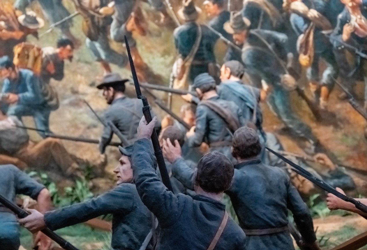Historical battle scene painting showing soldiers in blue uniforms engaged in combat.