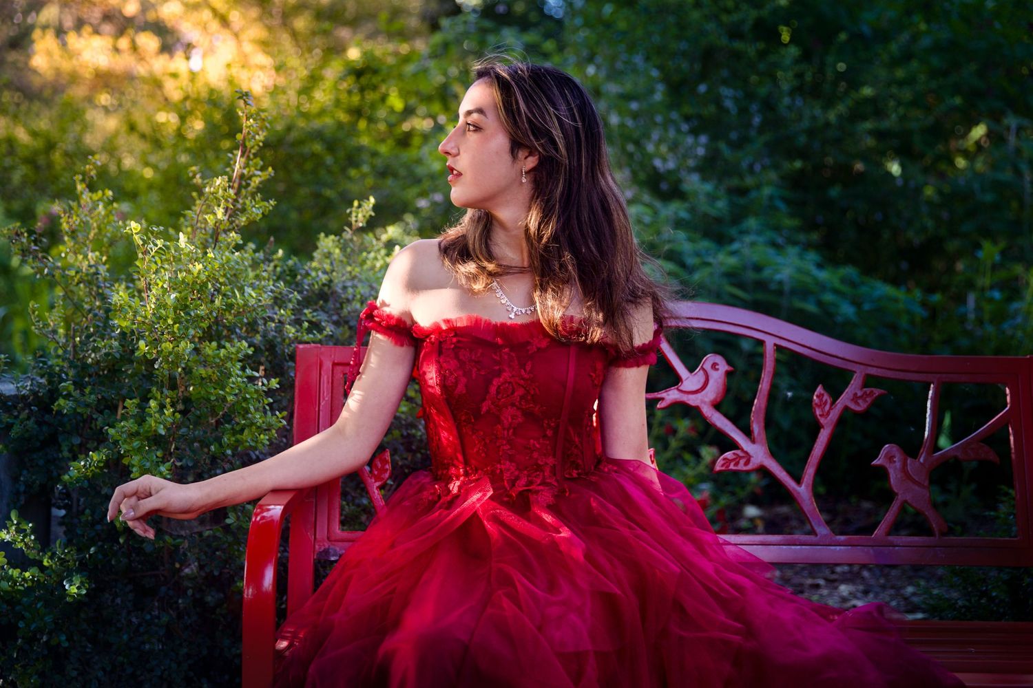 A girl in a red dress poses on a bench and looks to the left. Bay Area prom portrait
