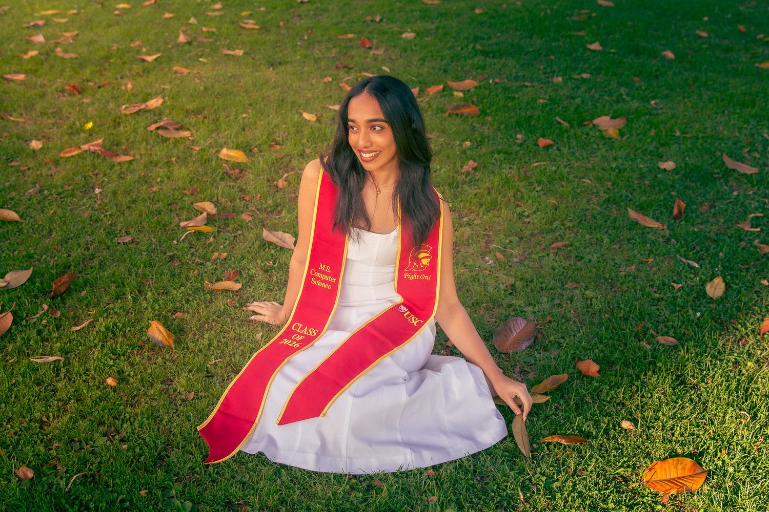 A girl in a pink gown stands underneath a leafy arch and smiles. Bay Area prom portrait