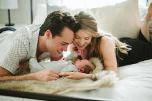 Parents sharing an intimate moment with their newborn on a white bed.