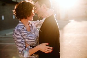 Couple embracing in warm sunlight against urban backdrop during romantic sunset moment.