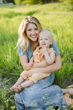 A parent and child share a joyful moment sitting in a sunny meadow.