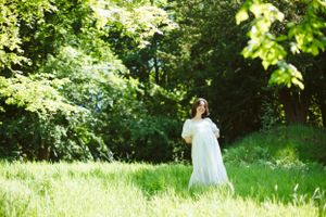 A figure in white dress walking through a sunny meadow surrounded by lush greenery.