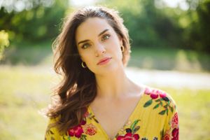 A person in a yellow floral dress poses in golden summer light.
