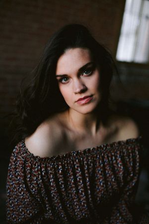 Portrait of someone wearing an off-shoulder floral top in moody indoor lighting.