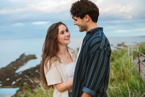 A romantic couple shares an intimate moment on a coastal clifftop during golden hour.