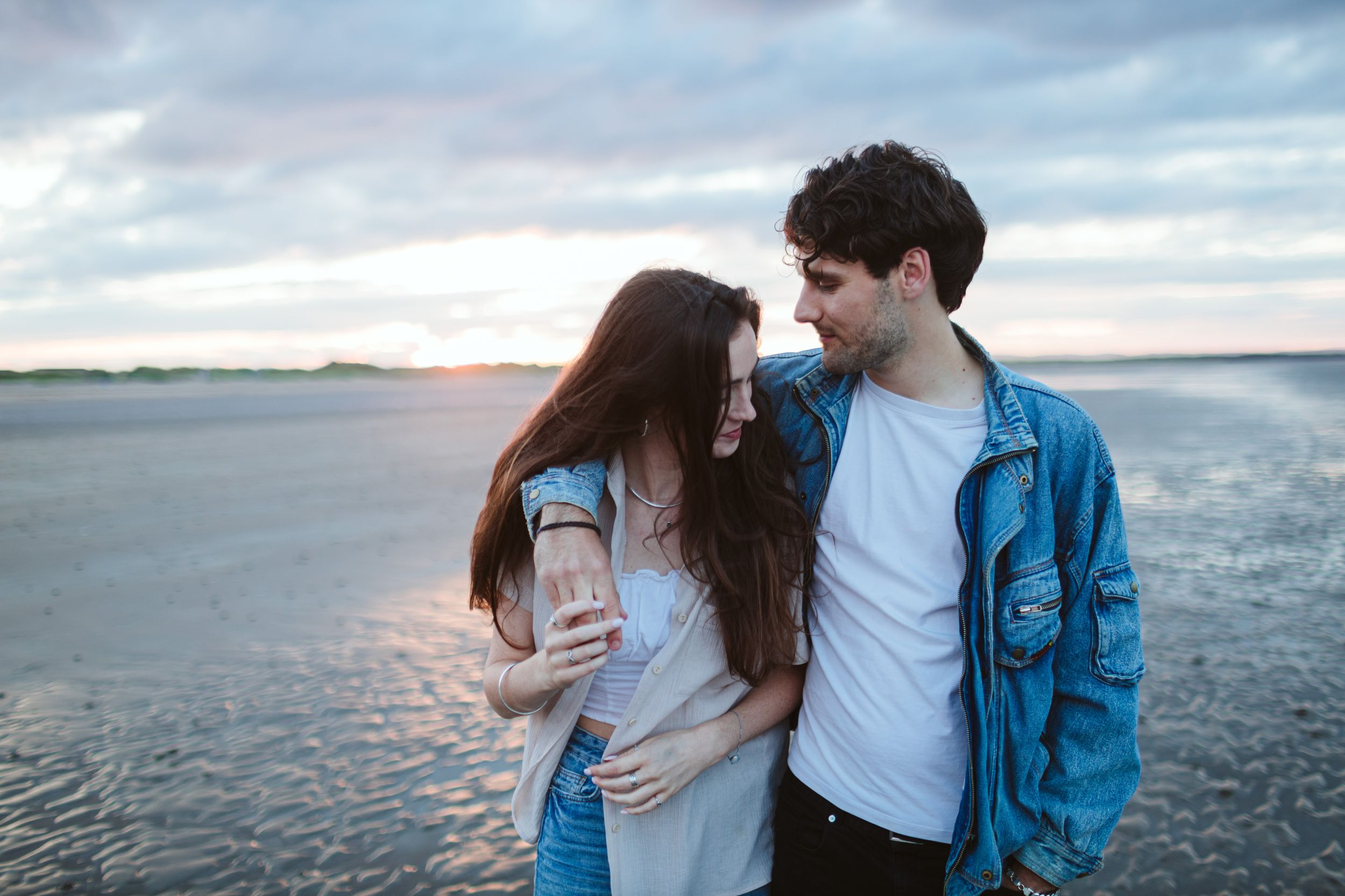 A couple embraces by the waterfront during a moody sunset.