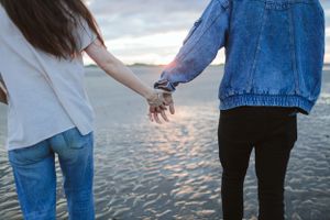 Close up of two people holding hands by the water at sunset.