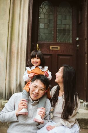 A joyful family moment captured on stone steps with a child sitting on parent's shoulders.
