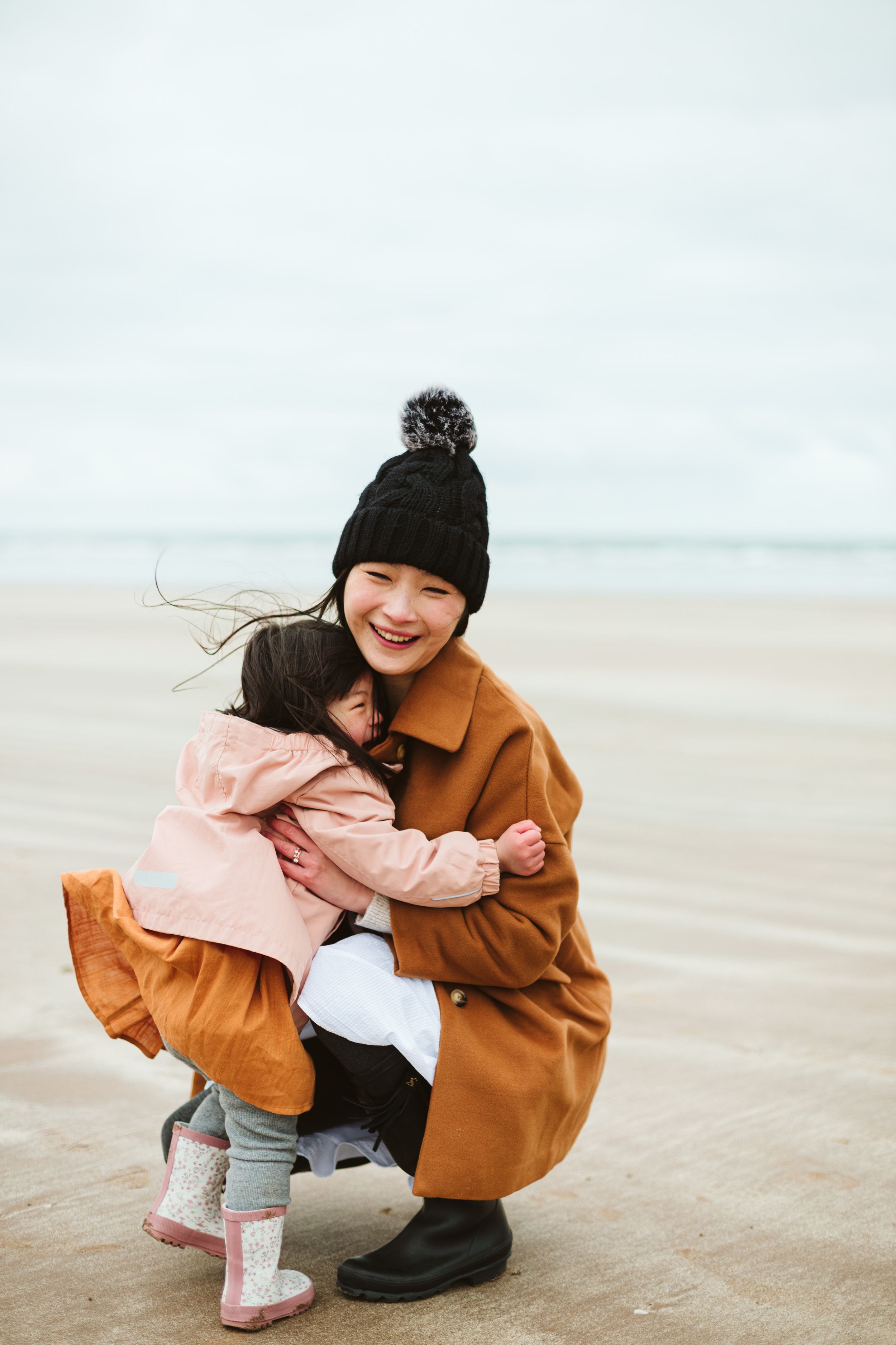 A parent and child share a joyful moment on a cloudy beach.