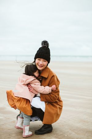 A parent and child share a joyful moment on a cloudy beach.