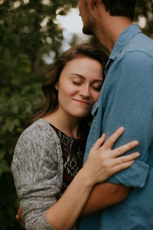 Tender embrace captured in natural setting with soft lighting and foliage.