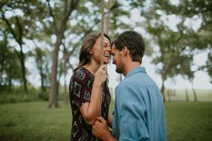 Couple sharing intimate moment outdoors in green field with trees in background.