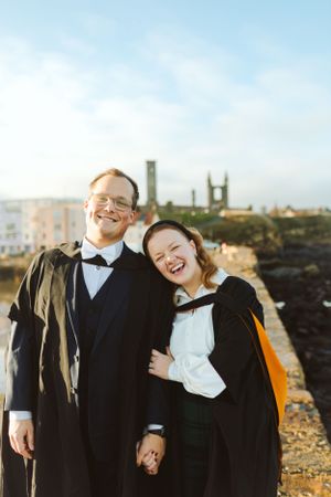 Two graduates in academic robes share a happy moment on campus.