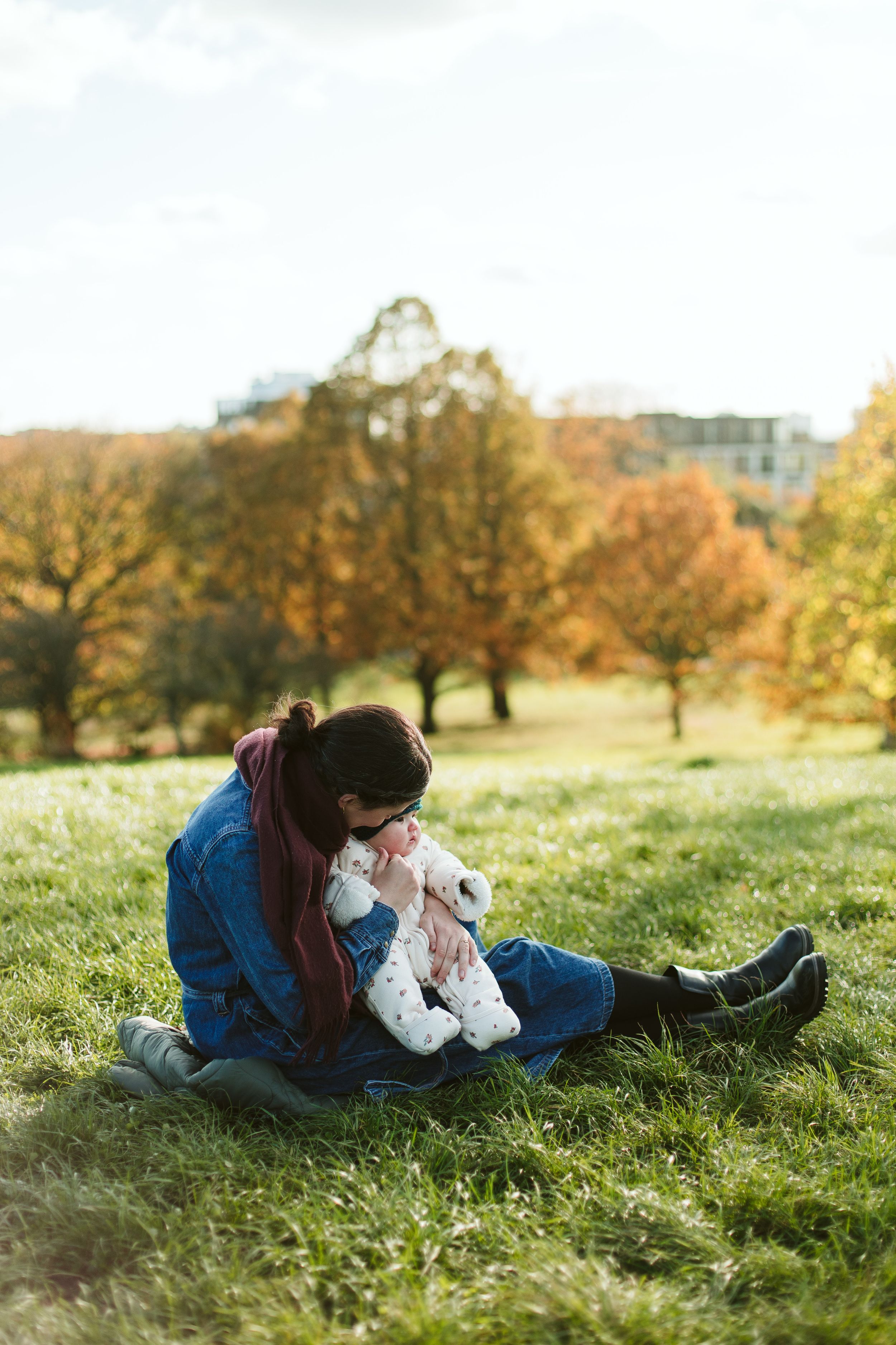 A parent and child share a tender moment while sitting on autumn grass.