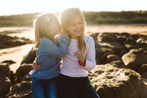 Two children share a sweet moment on rocky coastal terrain at sunset.