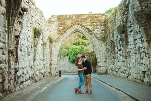 A couple embraces under an ancient stone archway on a historic street.