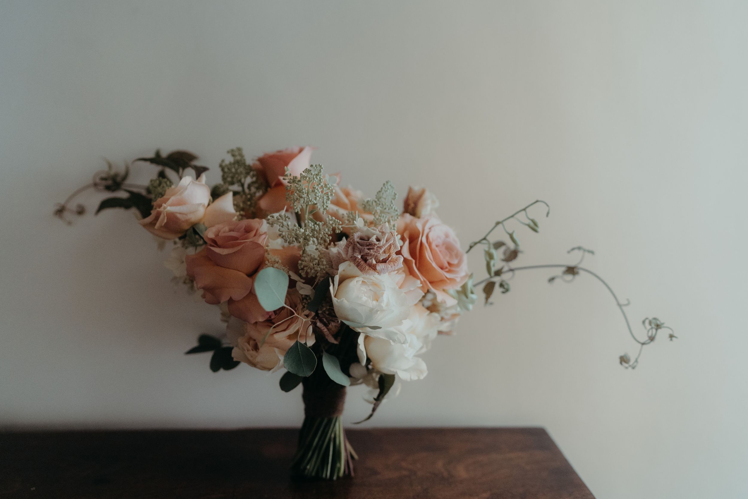 Romantic pastel bouquet with roses and eucalyptus on wooden surface.