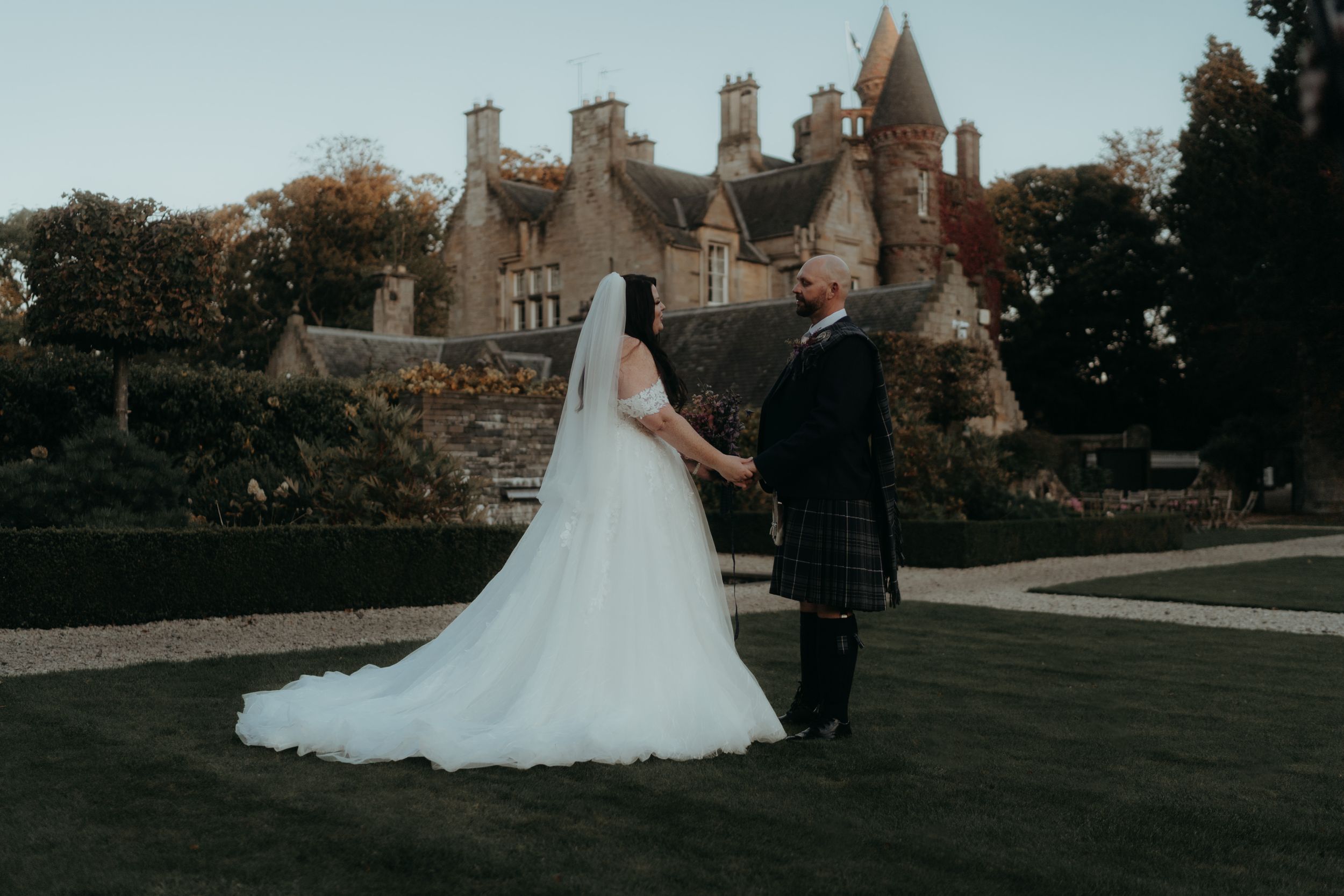 Wedding couple poses in front of a grand castle-like venue with gothic architecture at sunset.