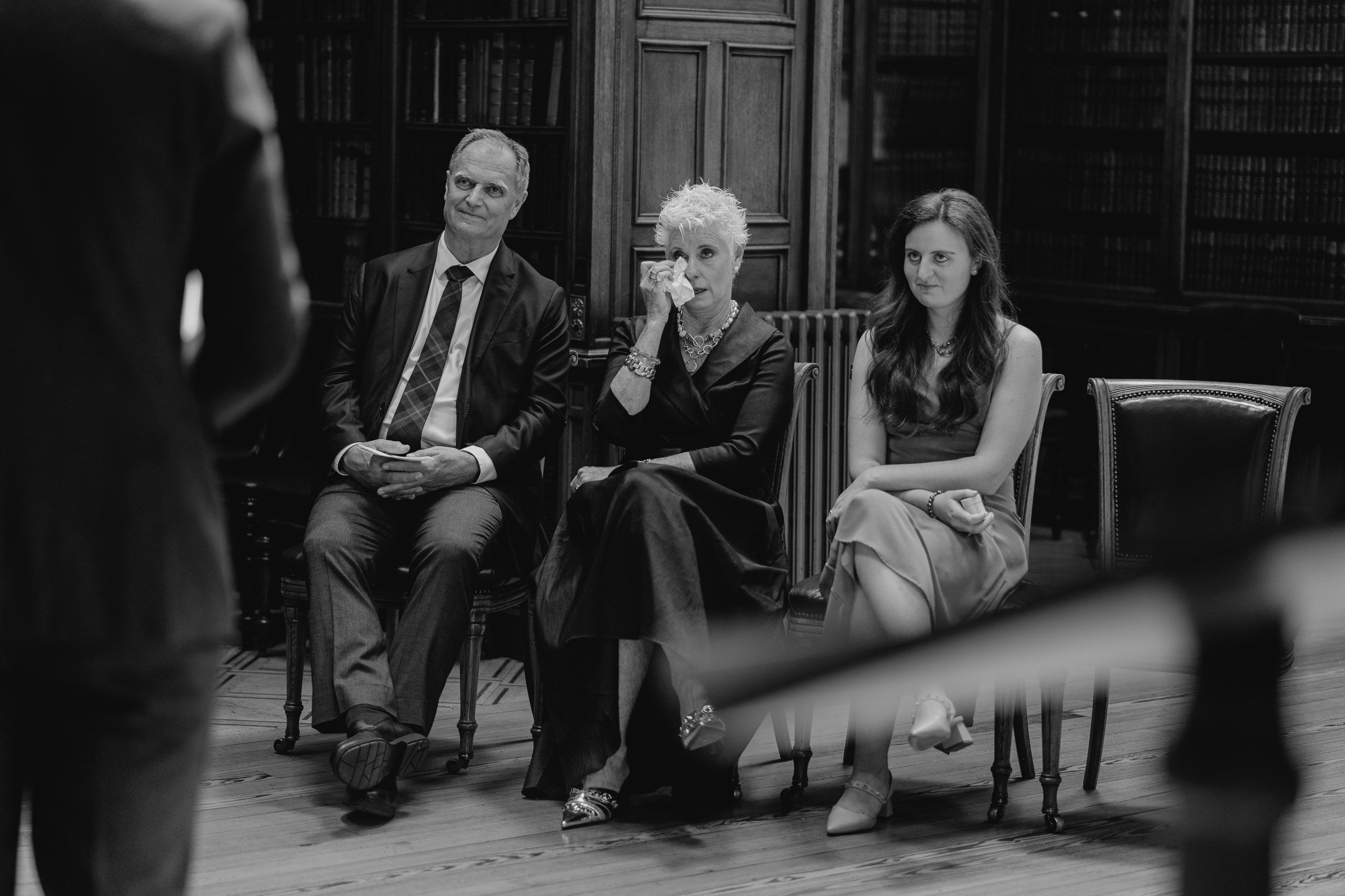 Black and white photo of three people seated during an indoor gathering.