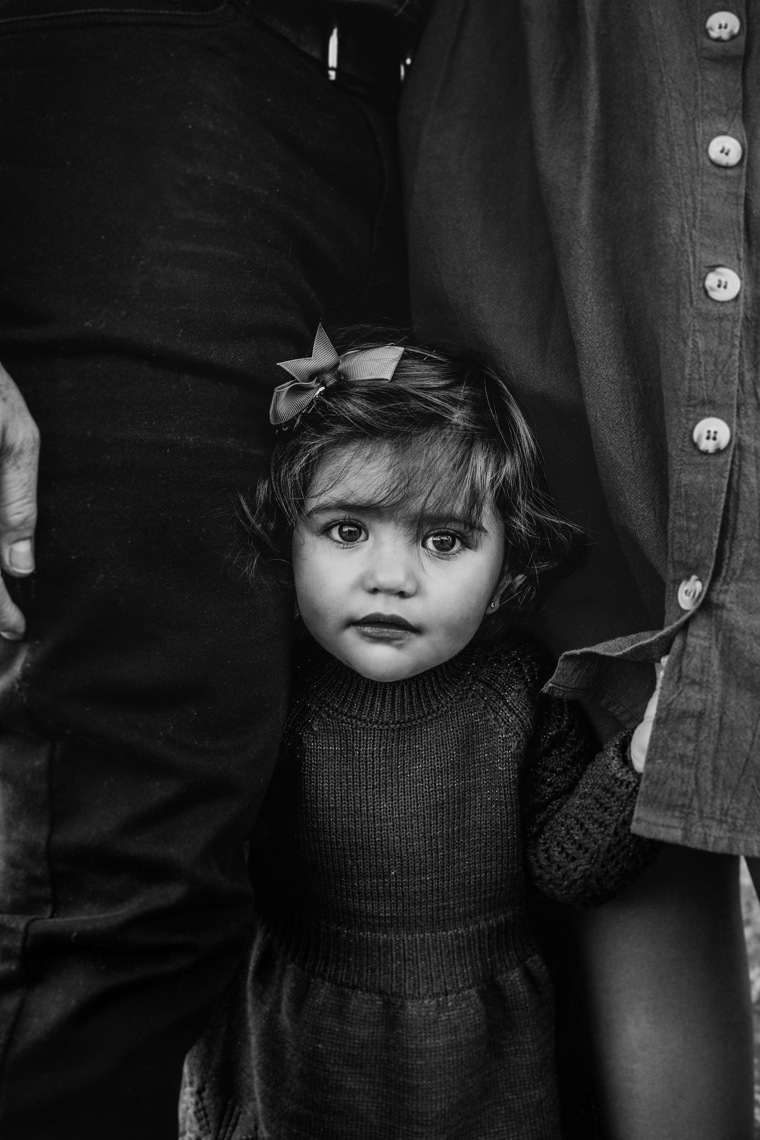A black and white portrait of a small child between two adults.