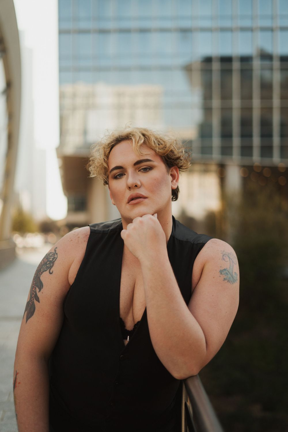 Portrait of person in black sleeveless top posing outdoors with urban background.