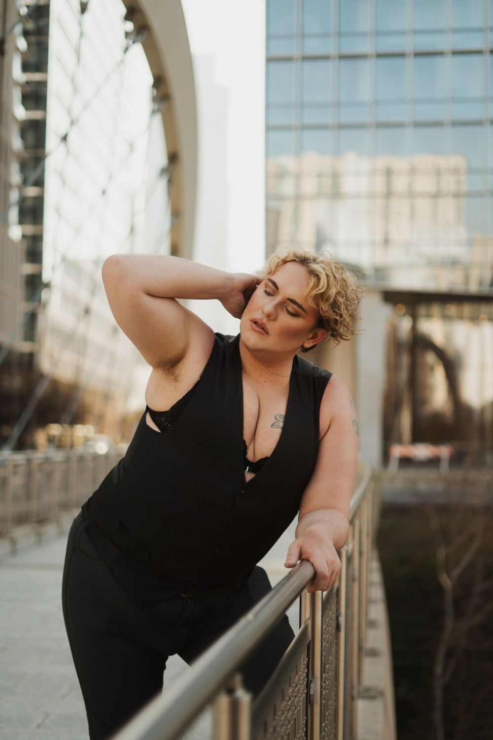 Artistic portrait of person in black outfit posing along urban railing at sunset.