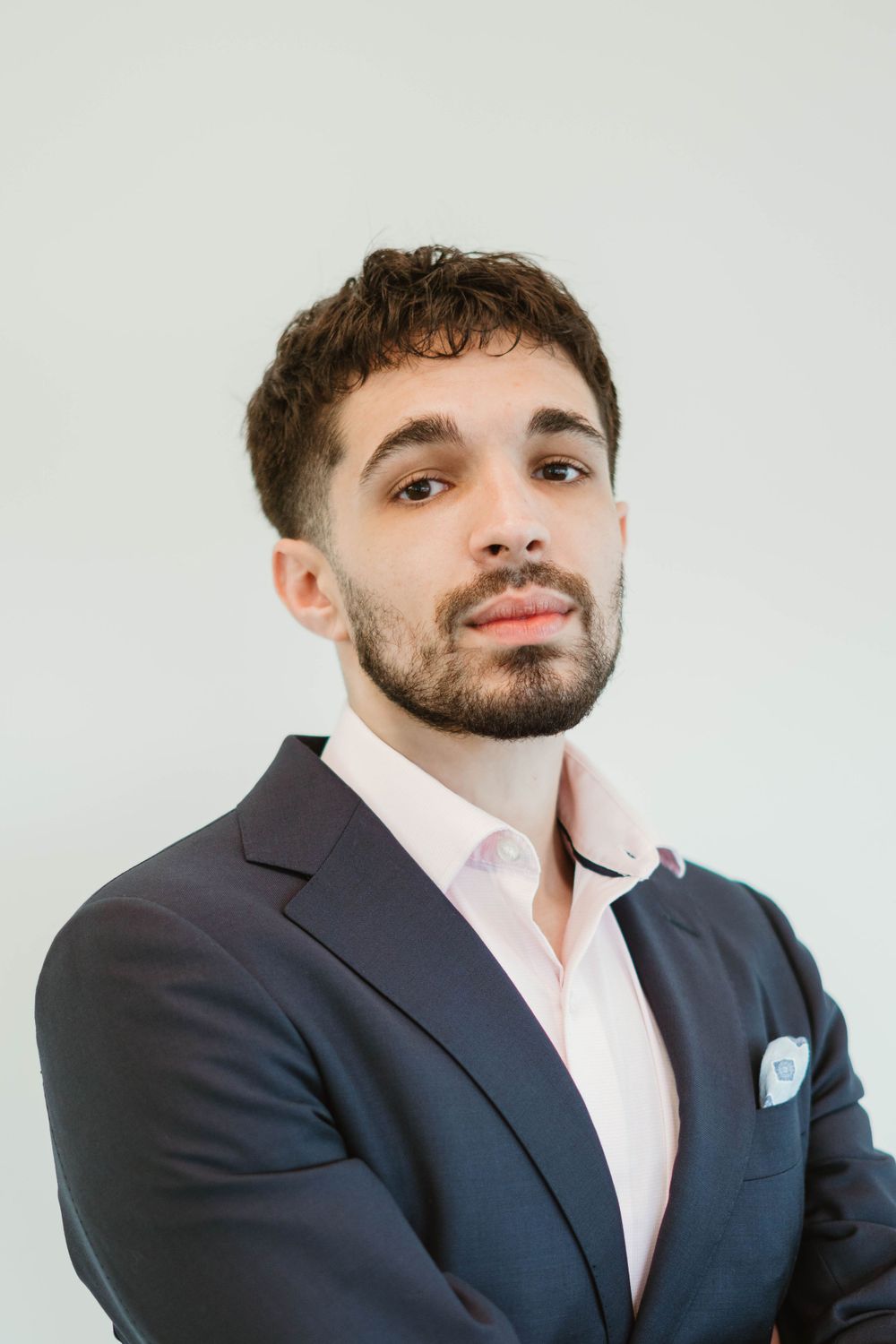 Professional headshot of person in navy suit with pink dress shirt against white background.