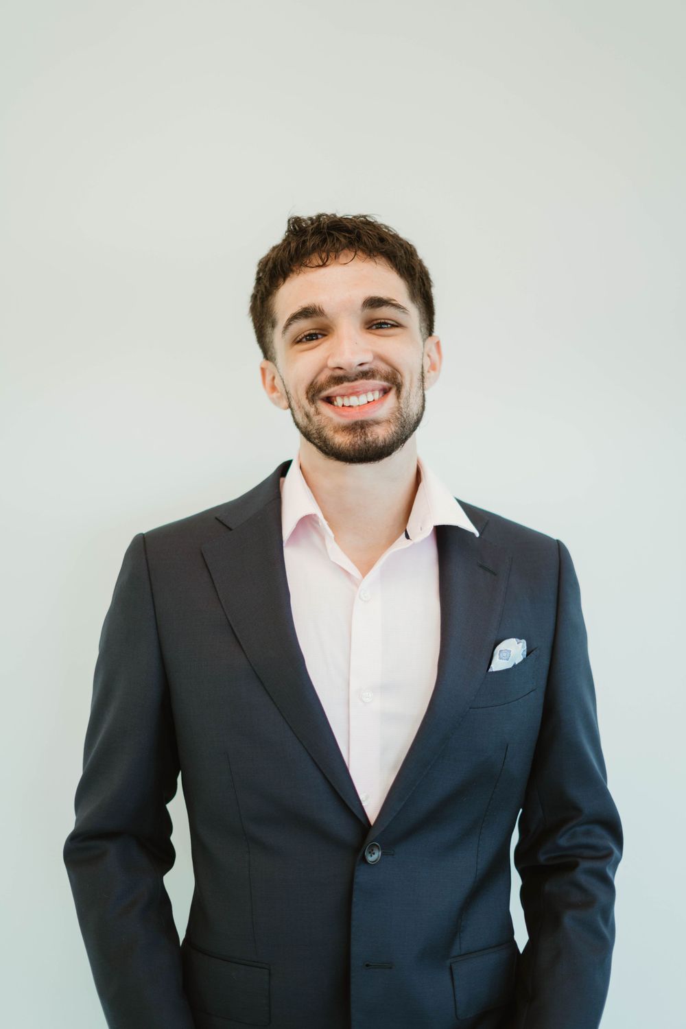 Professional portrait of person in dark suit smiling against light background.