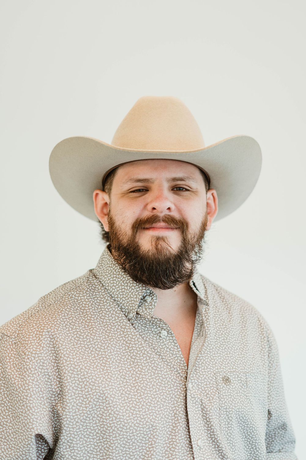 Close-up portrait of person wearing beige cowboy hat and patterned shirt.