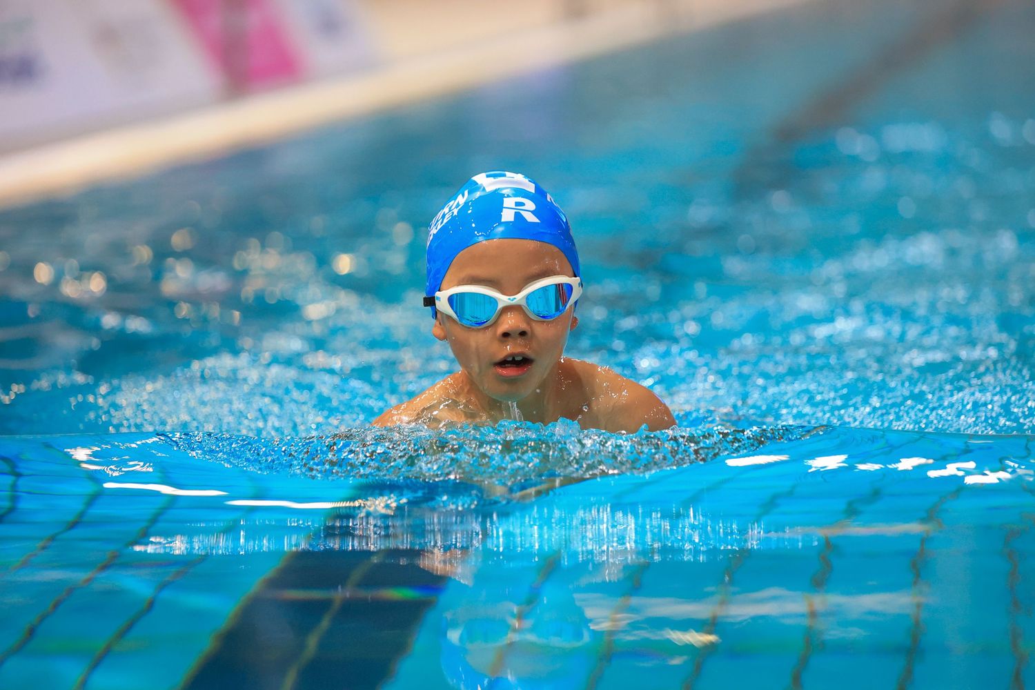 Competitive swimmer performing breaststroke in a pool wearing blue swim cap and goggles.