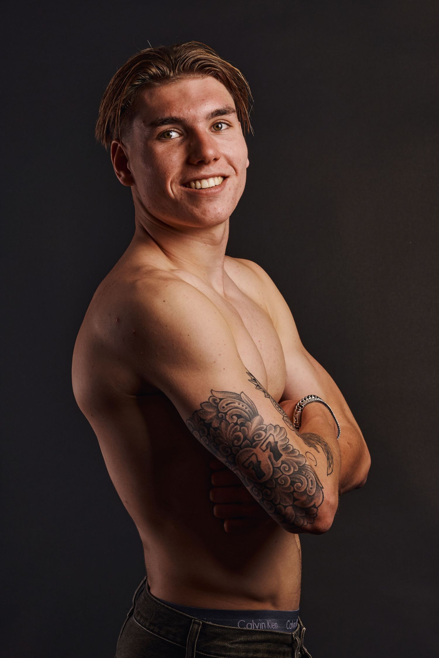 Jonge man zonder shirt met armen gekruist en tattoos en een zelfverzekerde glimlach