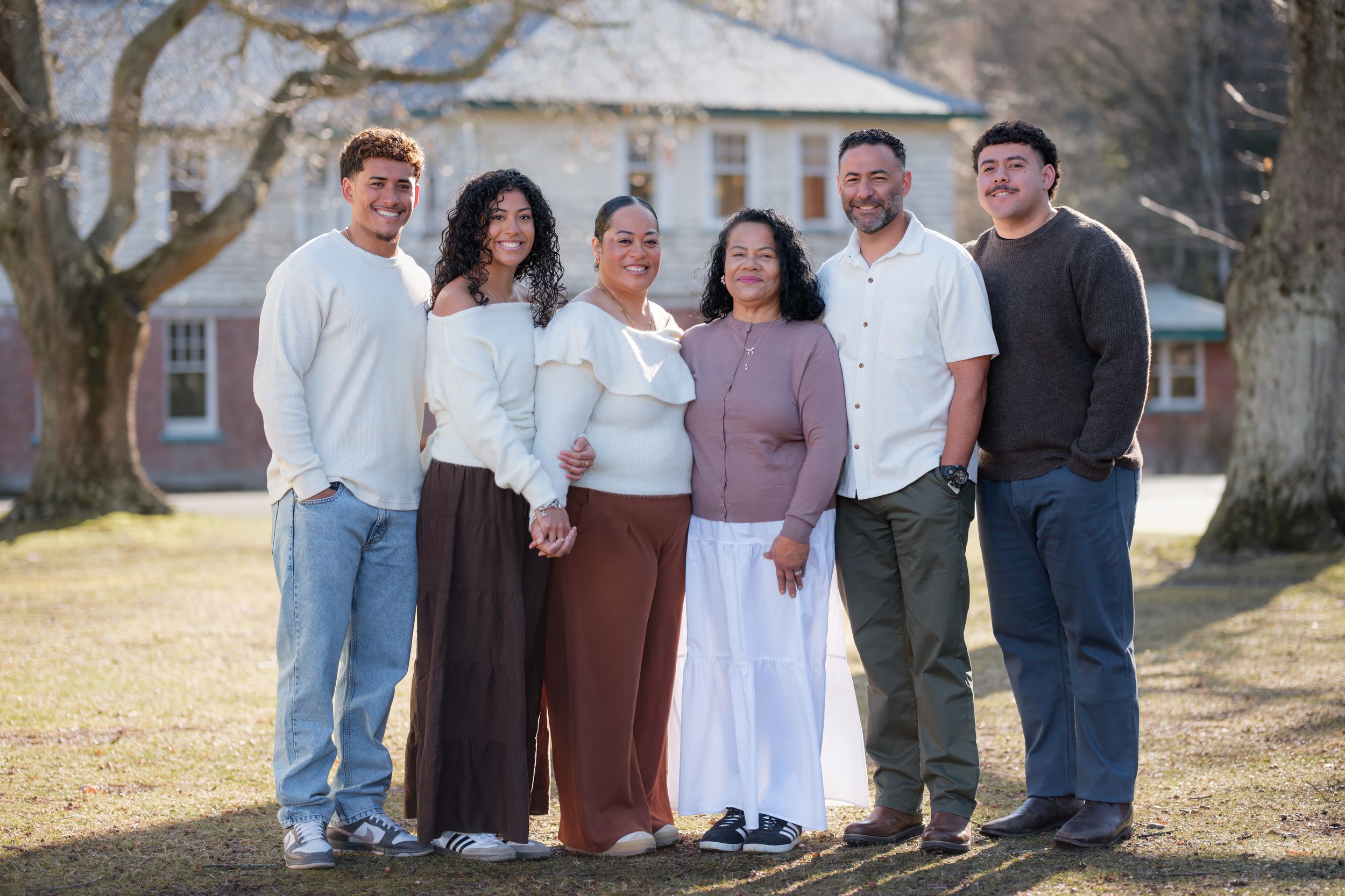 Family group portrait taken outdoors with traditional brick building in background. queen Mary hospital, Hanmer Springs.
