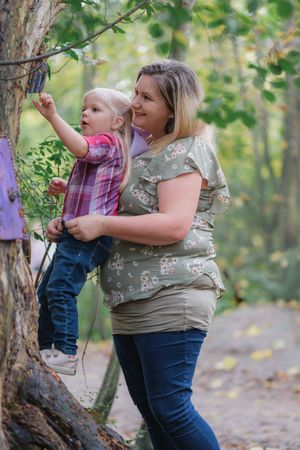 Parent and child exploring nature together near a tree in a forest setting.