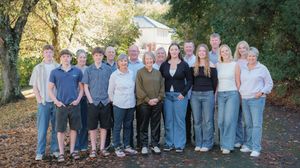 Panoramic family group photo with multiple generations posed in casual outdoor setting.