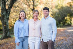 Family portrait taken outdoors during autumn with fall foliage in the background.